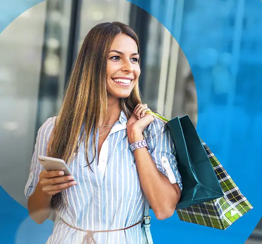 Omnichannel Hauptbild: Eine Frau mit einem Handy in der Hand und einer Einkaufstasche über der Schulter hat ein tolles Einkaufserlebnis